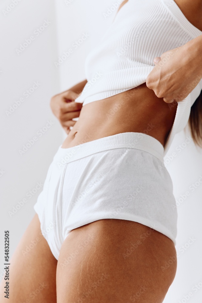Fototapeta premium A beautiful woman model with tanned skin and a beautiful slender body close-up posing on a white background. Body care and skin health concept with spf