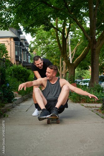 Male pushing same sex partner on skateboard.