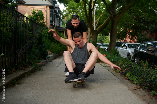 Male pushing same sex partner on skateboard.