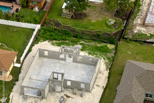 Aerial view of unfinished frame of private house with brick concrete walls ready for mounting wooden roof beams under construction