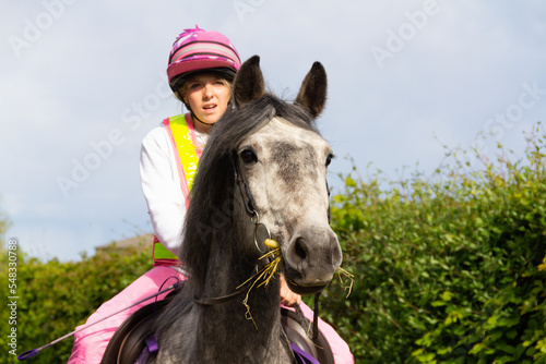 Close up shot of beautiful grey horse and her pretty young female rider as they enjoy riding freely in the English countryside on a summers day.