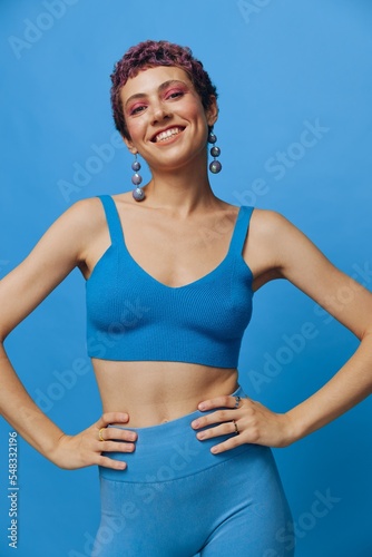 Young athletic fashion woman posing in blue sportswear smiling and looking at the camera on a blue monochrome background