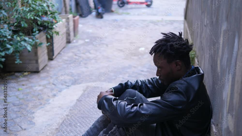 Depressed African man sitting on street, male white hand helping him standing Depressed African man sitting on street, male white hand helping him standing