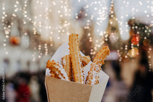 Close up churros on traditional Christmas fair in snow. Enjoying sweets on Xmas market. Winter holidays with family. Merry Christmas.