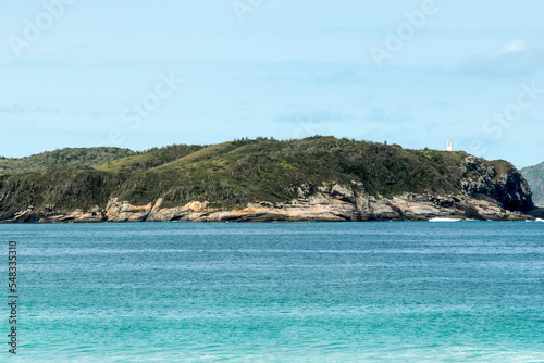 Orla do Chateau Recanto das Dunas na Praia das Dunas, com ondas fortes, lindo céu azul e farol encima de rochedo.