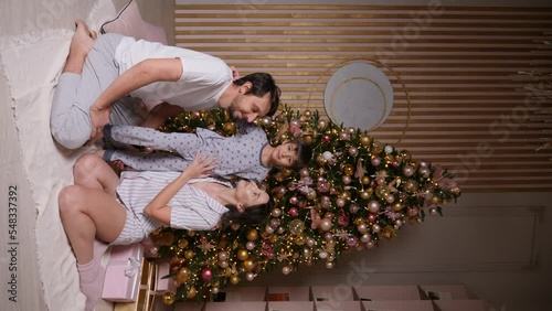 family with a baby boy in pajamas is sitting at the Christmas tree in the new year at home. Vertical. people are looking at the camera