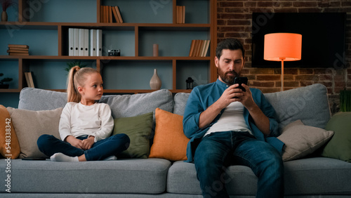 Bored child girl resting at home with father young dad using mobile phone little kid need attention looking at daddy taking modern gadget young family generation internet technology addiction concept
