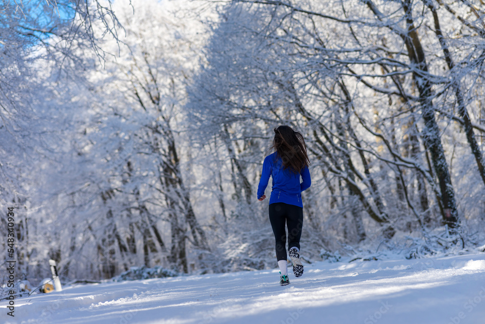 Sportswoman running in nature at snowy winter day. Winter fitness concept.