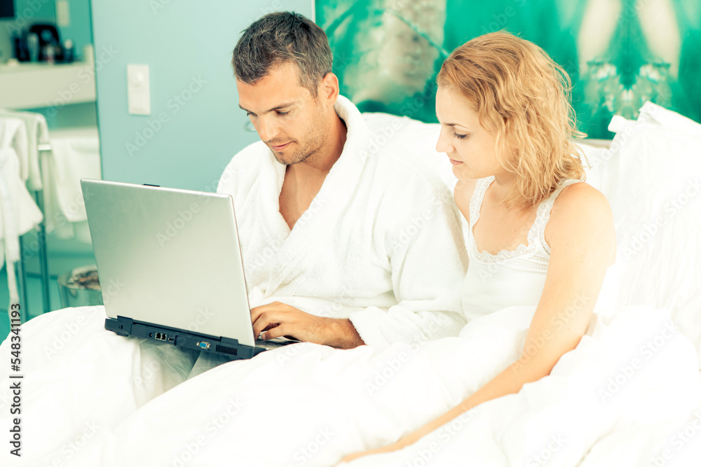 Fototapeta premium Young Couple with the laptop in the bed early morning checking email or social network