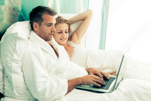 Young Couple with the laptop in the bed early morning checking email or social network