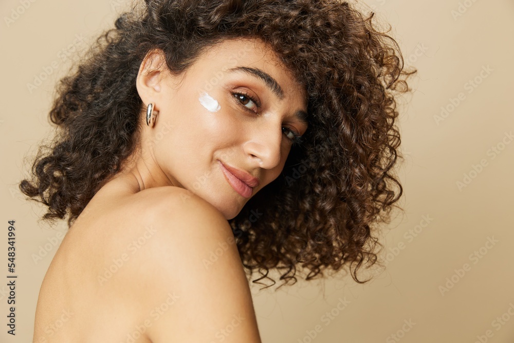 Woman beauty face close-up applying anti-aging moisturizer with fingers of her hand, skin health nails and hair, hair dryer style curly afro hair, body and beauty care concept Woman beauty face close-up applying anti-aging moisturizer with fingers of her hand, skin health nails and hair, hair dryer style curly afro hair, body and beauty care concept