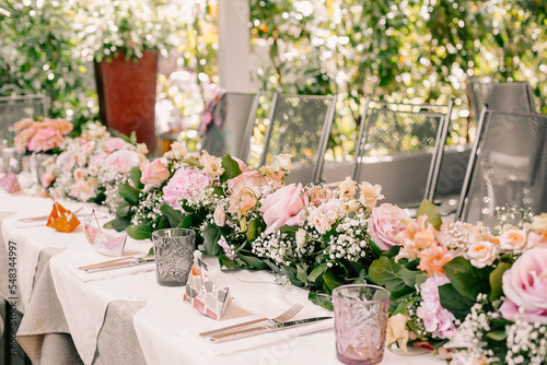 Festive table prepared for banquet with flower decorations, glassed cutlery and glasses outdoors during sunny day