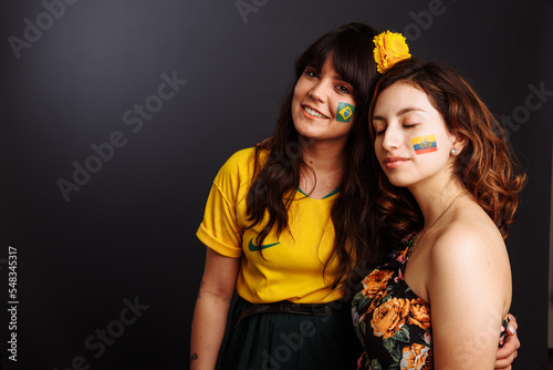 Brazilian and Ecuadorian ladies with body art on their faces looking forward surprized. Colorful painting. Selective focus