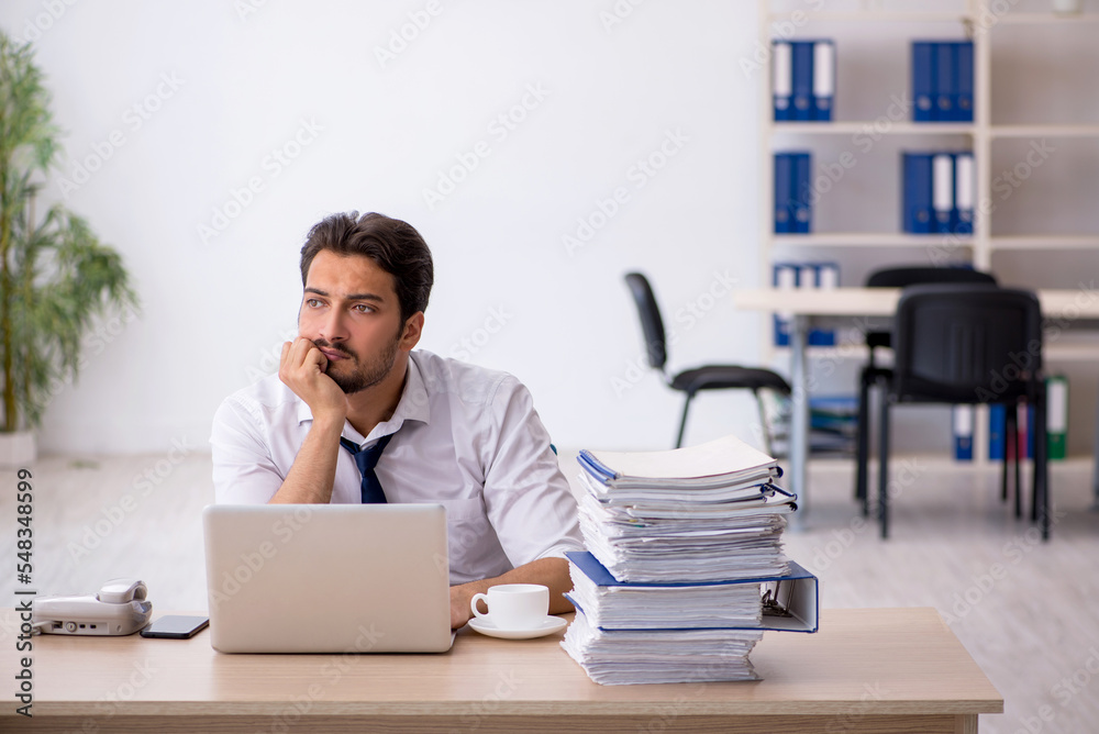 Young male employee unhappy with excessive work in the office Young male employee unhappy with excessive work in the office