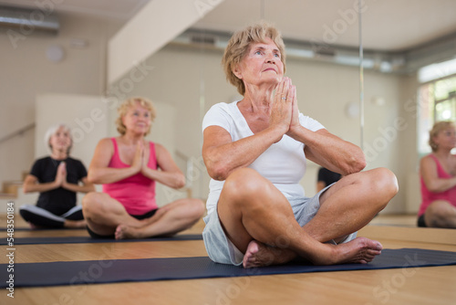 Active mature women practicing yoga in a group training session perform the exercise while sitting in the lotus position