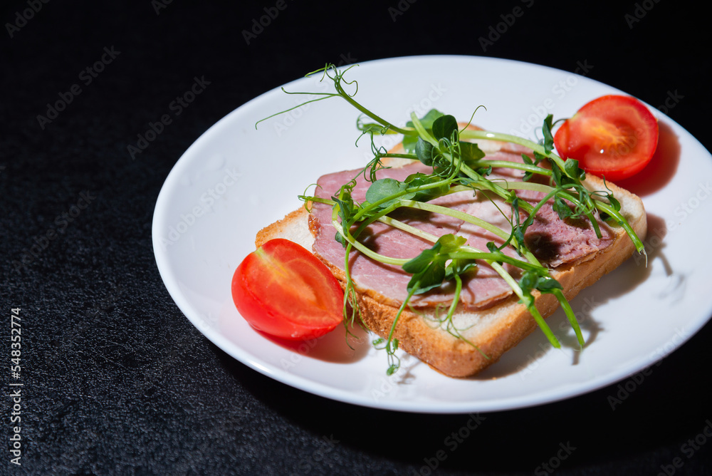 sandwich with bacon and microgreens and tomatoes on a black background