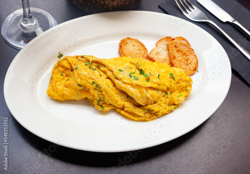Appetizing fluffy french omelet stuffed with cheese and greens served with browned toasts