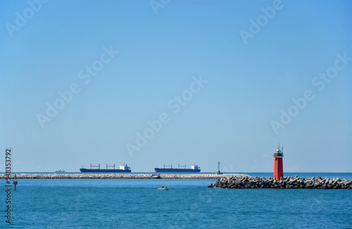 Cargo ships in blue sea and lighthouse on the pier