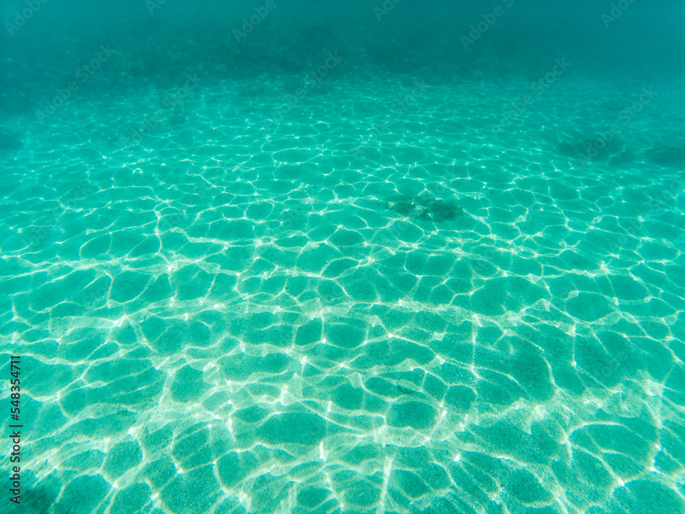 Underwater picture of sand sea bottom with waves refraction visible on the sea floor