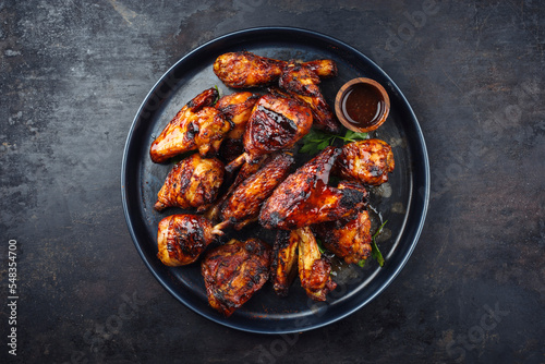 Traditional barbecue chicken wings and drumsticks with hot chili mango sauce and coriander served as top view on a rustic plate with copy space