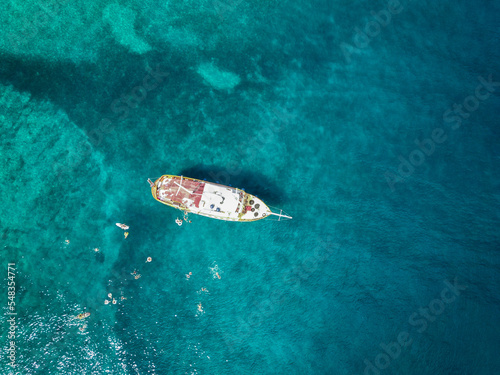 Aerial top down view of tourist ship anchored in the amazing, turquoise shallows of Brac island, Croatia with people swimming in the water