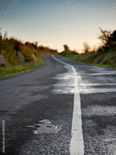 Small narrow asphalt road in a country side with slight damage to surface at sunset. Nobody. Selective focus. Travel and tourism concept.