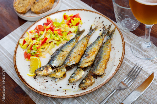 Appetizing fried sardines with a light vegetable salad made from lettuce, tomatoes and red pepper. Decorated with a slice ..of lemon