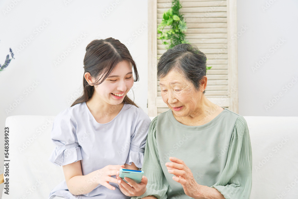 家でスマホを使う孫と祖母 家でスマホを使う孫と祖母