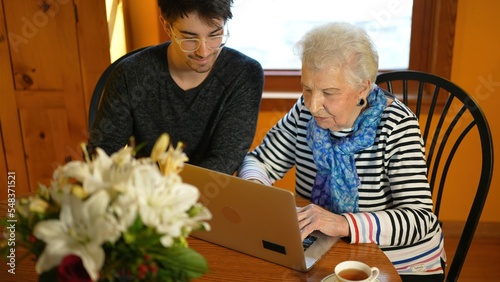 Overhead view of happy senior elderly woman sitting with teen grandson learning to use laptop computer in dining room.