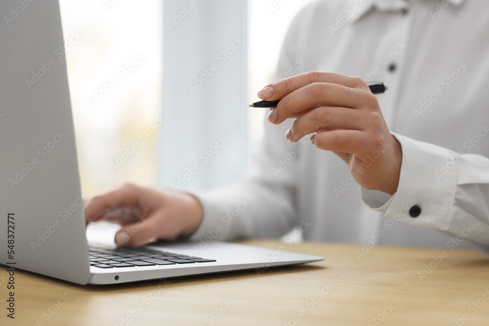 Woman with pen working on laptop at wooden table, closeup. Electronic document management Woman with pen working on laptop at wooden table, closeup. Electronic document management