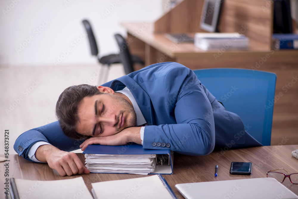 Young male employee unhappy with excessive work in the office Young male employee unhappy with excessive work in the office