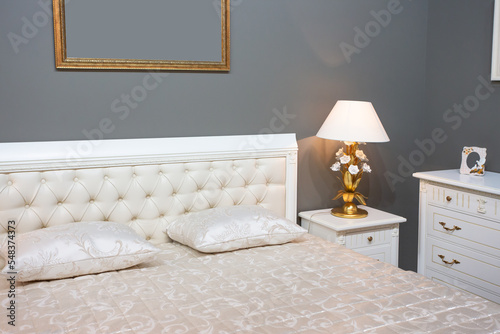 Luxury and expensive bedroom interior with white bad, golden lamp, ivory commode and golden frames