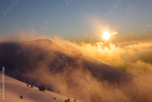 beautiful sunset over snowy alpine mountain with windy orange cloudy and foggy sky, Marmarosy, the Carpathian mountains