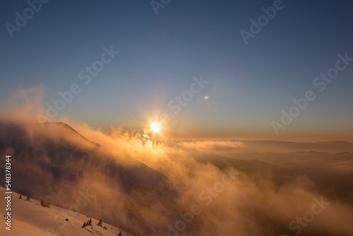 Sunset in a beautiful snowy alpine mountains with windy orange cloudy sky, Marmarosy, the Carpathians