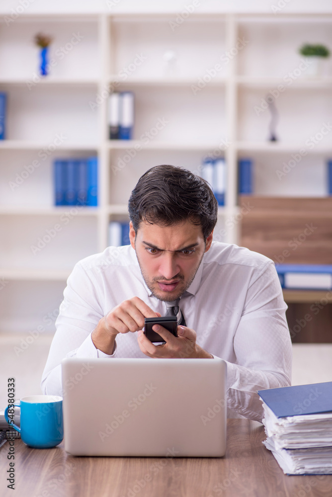 Young male employee unhappy with excessive work at workplace Young male employee unhappy with excessive work at workplace