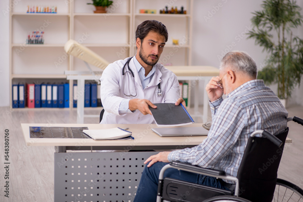 Old man in wheelchair visiting young male doctor Old man in wheelchair visiting young male doctor
