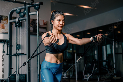 Asian woman doing exercises with crossover cable machine exercises in the gym. Fitness, healthy style concept.