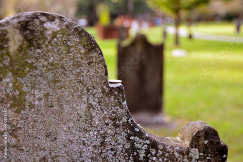 Close-up of old, worn tombstone in focus with a coin on it and a cemetery in the background