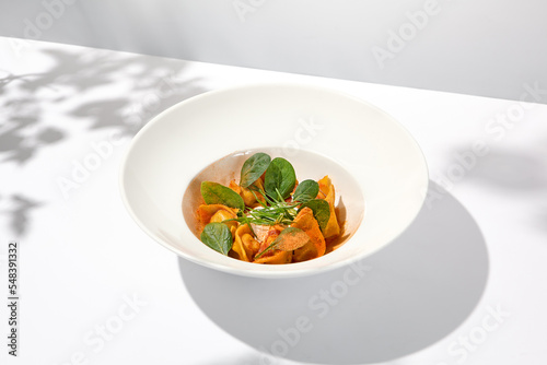 Tradition italian stuffed pasta - tortellini with minced meat. Italian ravioli on white background with harsh shadows. Summer menu italian restaurant. Tortellini with beef and spinach leaves