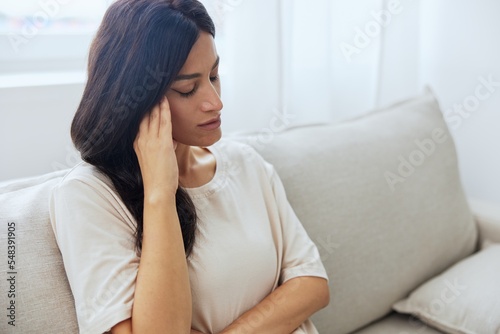 Headache woman sits at home on the couch and touches her head with her hands massage of the temples, high fever in case of illness, migraine