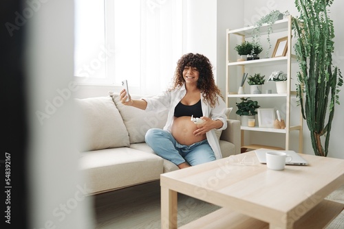 A pregnant woman blogger advertises a cream for pregnant women from stretch marks on the body during pregnancy filming herself on the phone while sitting on the couch at home freelancer