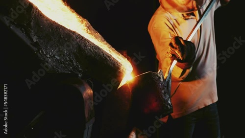 Process of hard working with hot melted metal from cast-iron furnace in foundry workshop. Anonymous strong man in protective clothes pours steel using special equipment