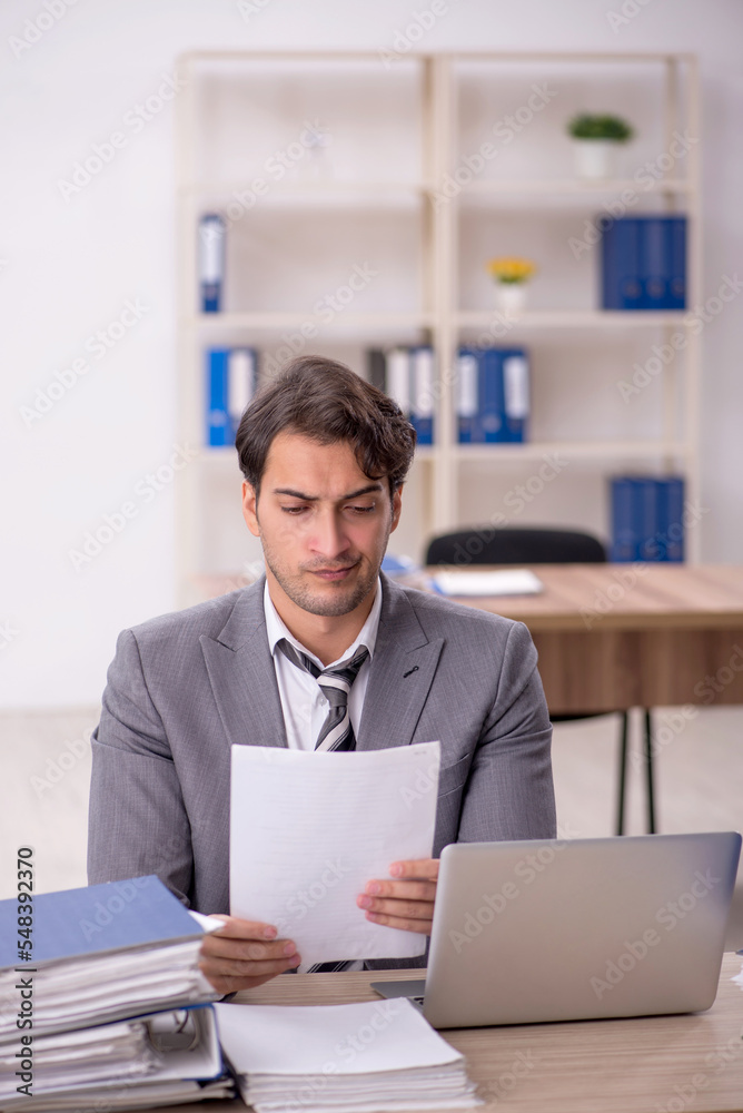 Young male employee unhappy with excessive work in the office Young male employee unhappy with excessive work in the office