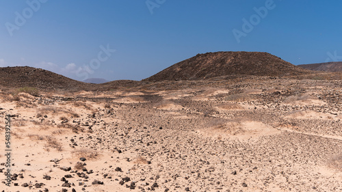 Wide light dry desert landscape with black volcanic rocks and elevations in distance