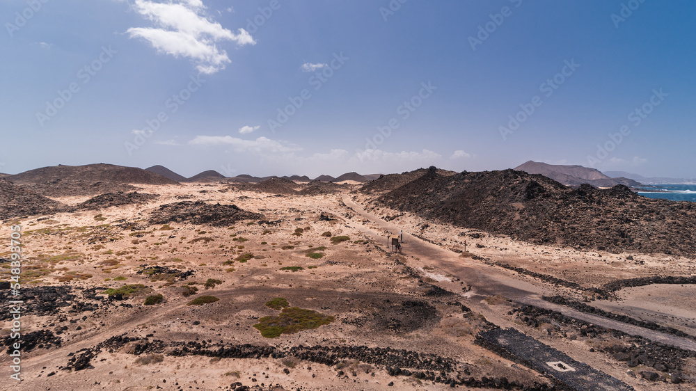 Volcanic hills surrounded by light colored sands with small road across Lobos Island, Spain