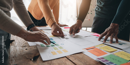 Close up ux developer and ui designer brainstorming about mobile app interface wireframe design on table with customer breif and color code at modern office.Creative digital development agency