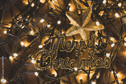 San Nicolás o papa Noel, en fondo de luces de navidad desenfocadas y letras doradas de Merry christmas, en fondo dorado, concepto de detalles y decoración navideña.  photo