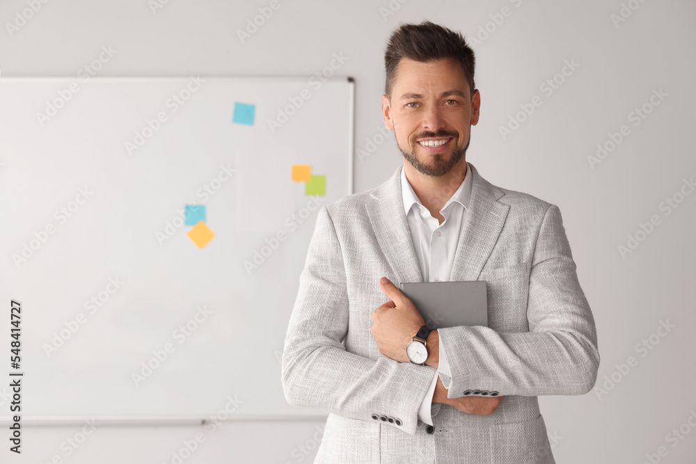 Happy teacher with book at whiteboard in classroom