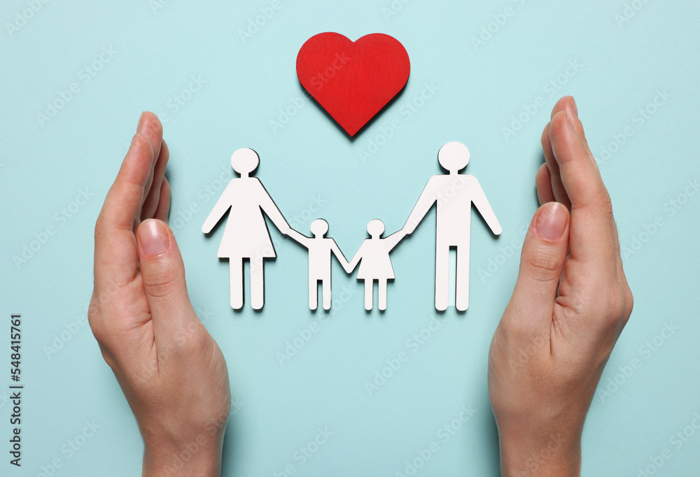 Woman protecting figures of family and heart on light blue background, top view. Insurance concept Woman protecting figures of family and heart on light blue background, top view. Insurance concept