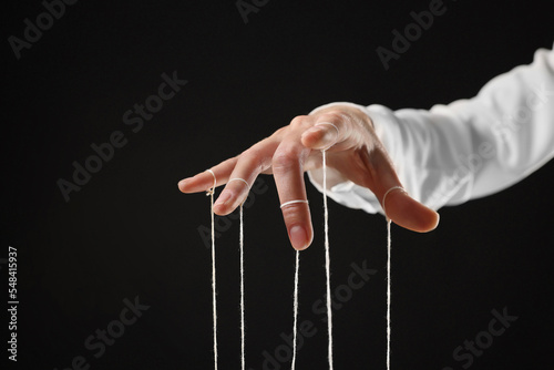 Woman pulling strings of puppet on black background, closeup photo